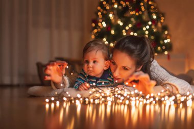 Anne ve bebek Noel arifesini evde güzel dekore edilmiş bir Noel ağacının yanında yatarak ve Noel ışıklarıyla oynayarak geçiriyorlar.