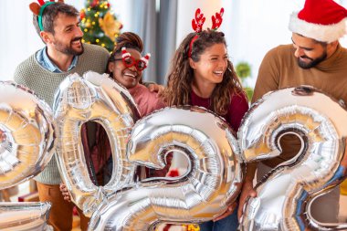 Bir grup genç arkadaş, 2022 numaralı dev balonları tutarak evde yeni yılı kutluyor.