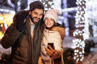 Güzel, genç bir çift arkadaşlarıyla video görüşmesi yapıyor. Yılbaşı gecesini arka planda bir sürü yılbaşı ışıklarıyla kutlarken akıllı telefonlar kullanıyorlar.
