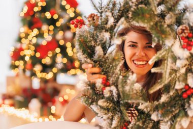 Güzel genç bir kadın Noel için evi dekore ederken eğleniyor, Noel çelengini tutuyor ve dikizliyordu.