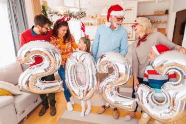Güzel mutlu bir aile Noel 'i evde kutluyor, 2023 numaralı dev balonları tutarak eğleniyor, gelecek yeni yılı temsil ediyor.