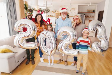 Güzel mutlu bir aile Noel 'i evde kutluyor, 2023 numaralı dev balonları tutarak eğleniyor, gelecek yeni yılı temsil ediyor.