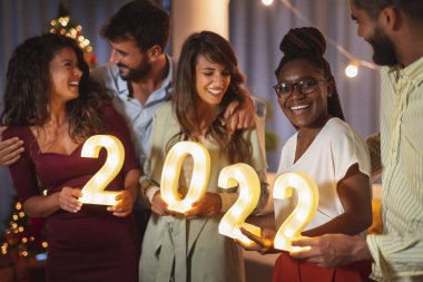 Yeni yıl partisinde eğlenen bir grup genç arkadaş, 2022 yılını temsil eden aydınlatıcı numaralar taşıyorlar.