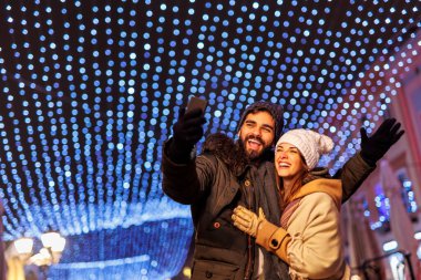 Güzel, genç ve aşık bir çift şehrin sokaklarında Noel arifesini kutlarken selfie çekerken eğleniyor.