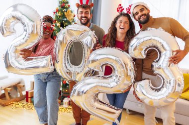 Bir grup genç arkadaş, 2023 numaralı dev balonları tutarak evde yeni yılı kutluyor.