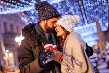 Genç ve güzel bir çift Noel arifesini dışarıda, sıcak sıcak sıcak şarap içerek ve kucaklaşarak geçiriyorlar.