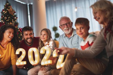 Mutlu bir aile yeni yıl arifesini evde çocuklarla birlikte kutluyor, Noel ağacının yanında oturuyor, ellerinde maytap ve 2022 numaralı aydınlatma numaraları var.