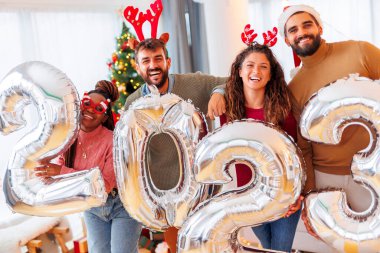 Yeni yılı evde kutlayan bir grup genç arkadaş, 2023 numaralı dev balonları tutarken yılbaşı partisi için hazırlanıyorlar.