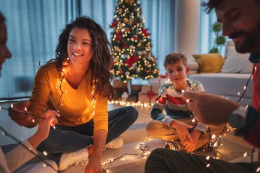 Aileler ve çocuklar yılbaşını evde kutlarken, Noel ağacının yanında yerde otururken, Noel ışıklarıyla oynarken eğleniyorlar.