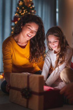 Anne ve kızı güzel dekore edilmiş Noel ağacının yanında oturuyor, sıcak ev atmosferinde kış tatilinin tadını çıkarıyor, parlayan Noel hediyesini açıyor.