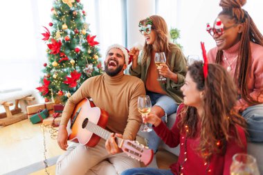 Bir grup arkadaş güzelce dekore edilmiş Noel ağacının yanında oturmuş, Noel 'i evde kutluyor, gitar çalıyor, şarap içiyor ve Noel şarkıları söylüyor.