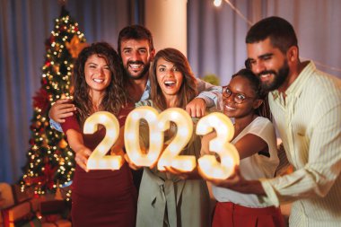 Yeni yıl partisinde eğlenen bir grup genç arkadaş, 2023 yılını temsil eden aydınlatıcı numaralar taşıyor.