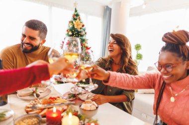Bir grup neşeli genç arkadaş kadeh kaldırıyor. Noel yemeği yerken ve Noel 'i evde birlikte kutlarken kadeh kaldırıyorlar.