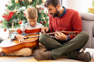 Baba oğluna Noel 'i evde beraber geçirirken gitar çalmayı öğretiyor. 