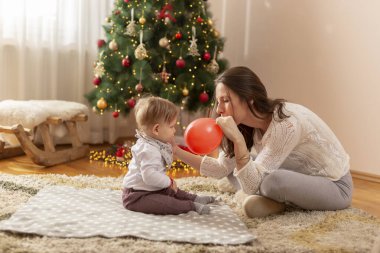 Anne ve oğlu Noel 'i kutlarken evde eğleniyorlar. Güzel dekore edilmiş Noel ağacının yanında oturup balon şişiriyorlar.