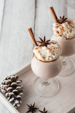 Anason yıldızı ve tarçın çubuklarıyla süslenmiş tarçın kenarlı bardaklarda servis edilen nefis ev yapımı kremalı eggnog manzarası - geleneksel kış tatili kokteyli