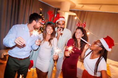 Bir grup genç arkadaş ellerinde maytap, şarkı söylüyor, dans ediyor ve yılbaşı partisinde ıslık çalıyor.