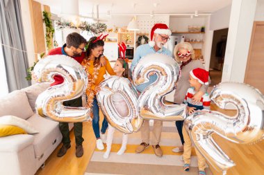 Güzel mutlu bir aile Noel 'i evde kutluyor, 2022 numaralı dev balonları tutarak eğleniyor, gelecek yeni yılı temsil ediyor.