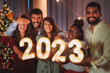Yeni yıl partisinde eğlenen bir grup genç arkadaş, 2023 yılını temsil eden aydınlatıcı numaralar taşıyor.