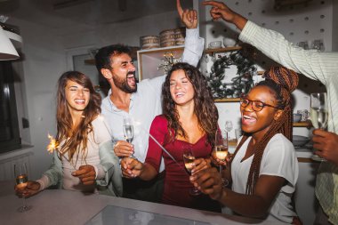 Bir grup genç arkadaş şarkı söylüyor, dans ediyor, maytap tutuyor ve yılbaşı partisinde şampanya içiyorlar.