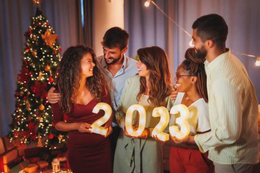 Yeni yıl partisinde eğlenen bir grup genç arkadaş, 2023 yılını temsil eden aydınlatıcı numaralar taşıyor.