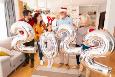 Güzel mutlu bir aile Noel 'i evde kutluyor, 2022 numaralı dev balonları tutarak eğleniyor, gelecek yeni yılı temsil ediyor.