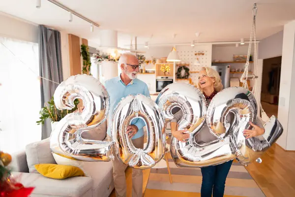 2022 numaralı büyük gümüş balonlar taşıyan yaşlı çift, yeni yılı temsil ediyor.