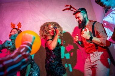 Bir grup neşeli genç arkadaş yeni yıl partisinde karaoke söyleyip dans ederek eğleniyorlar.