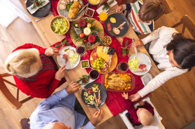 Masanın etrafında toplanmış mutlu, mutlu, çok nesilli aile manzarası, evde hep birlikte Noel yemeği yiyor, birbiriyle konuşuyor ve gülüyor.
