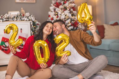 Güzel, genç ve aşık bir çift kış tatili için evi dekore ederken ellerinde 2024 numaralı balonlar olacak.