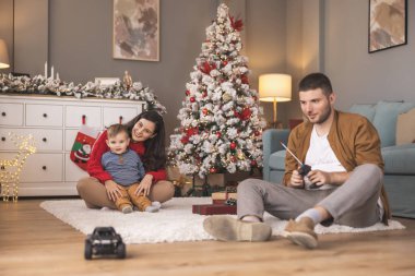 Genç ebeveynler, Noel 'i evde birlikte geçirirken hediyelerini açarken ve çocuklarıyla oynarken eğleniyorlar.