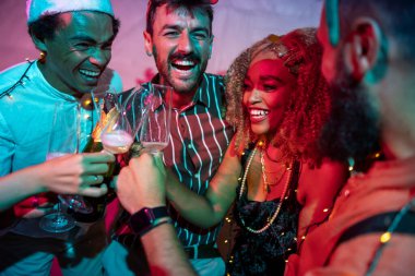 Bir grup neşeli genç arkadaş kadeh kaldırarak eğleniyor ve yılbaşı partisinde şampanya içiyorlar.