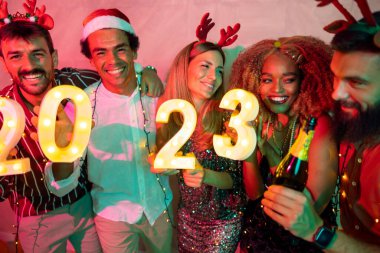 Yeni yıl partisinde eğlenen bir grup arkadaş, 2023 yılını gece yarısı geri sayımını temsil eden aydınlatıcı numaralar tutuyorlar.