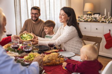 Mutlu çoklu nesil aile masanın etrafında toplandı, evde hep birlikte Noel yemeği yiyorlar, tabakları birbirlerine veriyorlar ve tabağa yemek koyuyorlar.