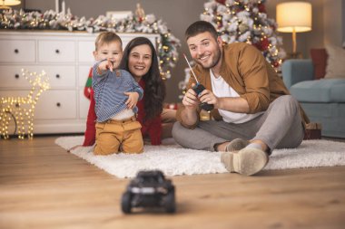 Genç ebeveynler Noel 'i evde birlikte geçirirken bebekleriyle oynarken eğleniyorlar. Çocuklar Noel oyuncak arabaları için heyecanlı.