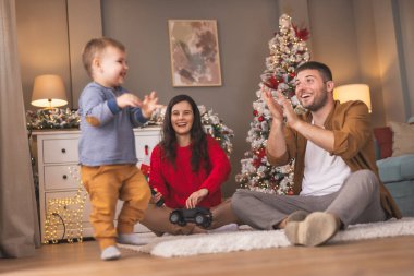 Genç ebeveynler Noel 'i evde yeni yürümeye başlayan çocuklarıyla birlikte geçiriyorlar, hediyeleri açıyorlar ve yeni oyuncaklarla oynuyorlar.
