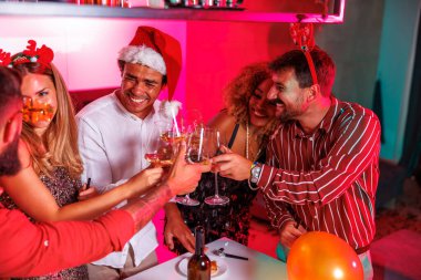 Bir grup neşeli genç arkadaş ev partisinde eğleniyor, kadeh kaldırıyor, şarap içiyor ve dans ediyor.