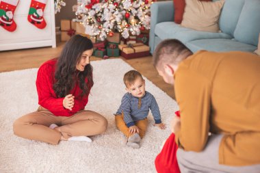 Genç ebeveynler Noel 'i evde birlikte geçirirken küçük çocuklarıyla birlikte Noel hediyelerini açarken eğleniyorlar.