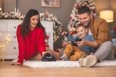 Genç ebeveynler Noel 'i evde birlikte geçirirken çocuklarıyla oynarken eğleniyorlar. Baba, oğluna uzaktan kumandalı oyuncak arabayı nasıl kullanacağını öğretiyor.