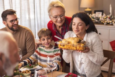 Mutlu aile masanın etrafında toplanmış, evde hep birlikte Noel yemeği yiyorlar, kadınlar masaya yemek koyuyorlar.
