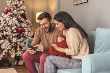 Güzel mutlu çift Noel 'i evde birlikte geçirip akıllı telefonlar kullanarak internette sörf yaparak eğleniyor.