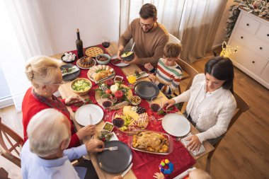Masanın etrafında toplanmış mutlu, mutlu, çok nesilli aile manzarası, evde hep birlikte Noel yemeği yiyor, birbiriyle konuşuyor ve gülüyor.