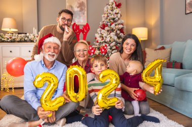 Güzel mutlu bir aile Noel 'i evde kutluyor, 2024 numaralı dev balonları tutarak eğleniyor, gelecek yeni yılı temsil ediyor.