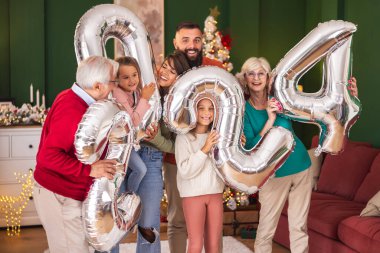 Güzel mutlu bir aile Noel 'i evde kutluyor, 2024 numaralı dev balonları tutarak eğleniyor, gelecek yeni yılı temsil ediyor.