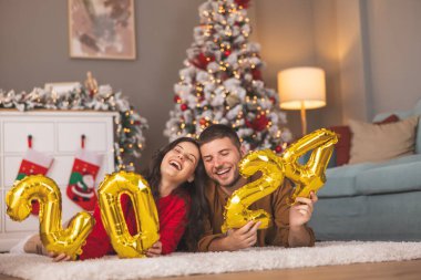 Güzel, genç ve aşık bir çift kış tatili için evi dekore ederken ellerinde 2024 numaralı balonlar olacak.