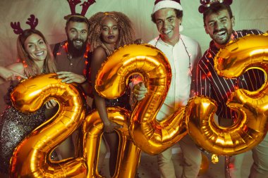 Bir grup genç arkadaş yeni yıl partisinde eğleniyor, dans ediyor ve gece yarısı geri sayımında 2023 numara şeklinde balonlar tutuyor.