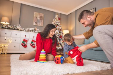 Genç ebeveynler Noel 'i evde birlikte geçirirken küçük çocuklarıyla birlikte Noel hediyelerini açarken eğleniyorlar.