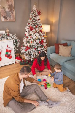Noel 'i evde birlikte geçirirken küçük çocuklarıyla oynayan genç ebeveynlerin yüksek açılı görüntüsü.