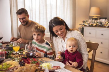Genç ebeveynler çocuklarıyla Noel yemeği yiyorlar. Aile tatilleri için evde toplanmış.