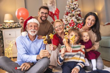 Güzel mutlu bir aile Noel 'i evde kutluyor, 2024 numaralı küçük balonları tutarak eğleniyor, yaklaşan yeni yılı temsil ediyor.